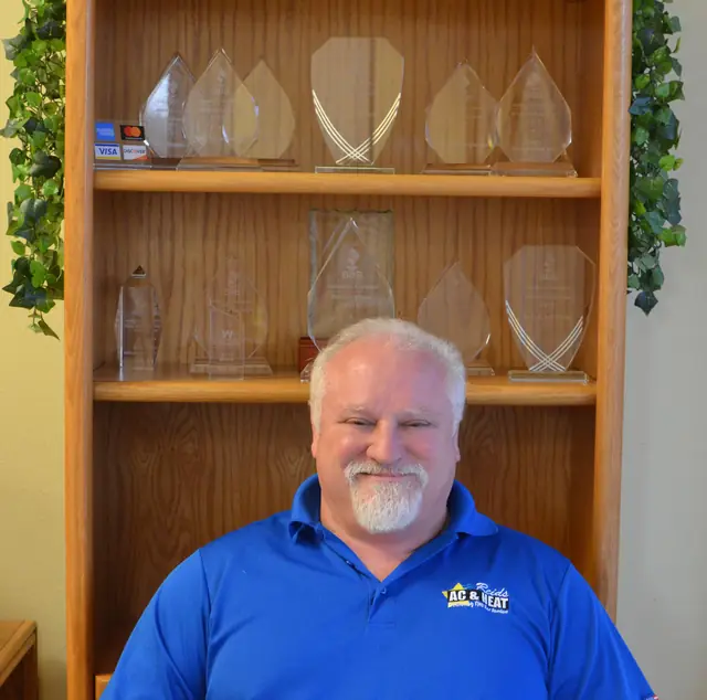 Reid Herring seated in front of the Reid's AC and Heating award shelf