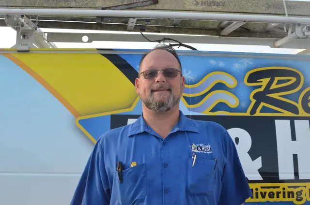 Reid's technician in a branded shirt standing beside the wrapped service van